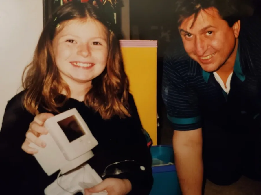 Ingrid as a child holding a small computer beside an adult