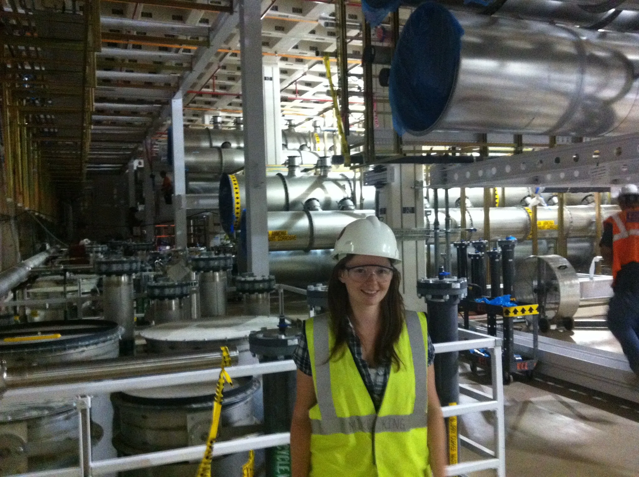 Ingrid wearing a hard hat, safety glasses, and a high-visibility vest in an industrial facility